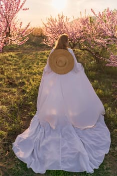 Woman blooming peach orchard. Against the backdrop of a picturesque peach orchard, a woman in a long white dress and hat enjoys a peaceful walk in the park, surrounded by the beauty of nature