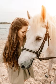 A white horse and a woman in a dress stand on a beach, with the sky and sea creating a picturesque backdrop for the scene