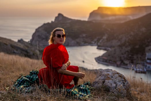 Woman sunset sea mountains. Happy woman siting with her back on the sunset in nature in summer posing with mountains on sunset, silhouette. Woman in the mountains red dress, eco friendly, summer landscape active rest.