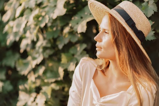 Woman with straw hat stands in front of vineyard. She is wearing a light dress and posing for a photo. Travel concept to different countries.