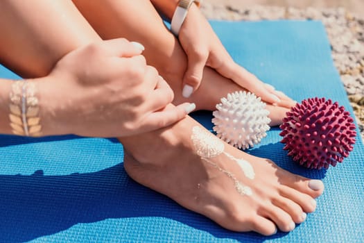 Middle aged well looking woman with black hair doing Pilates with the ring on the yoga mat near the sea on the pebble beach. Female fitness yoga concept. Healthy lifestyle, harmony and meditation.