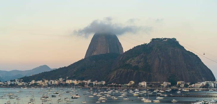 A scenic photo of Sugarloaf Mountain with boats on water during sunset.