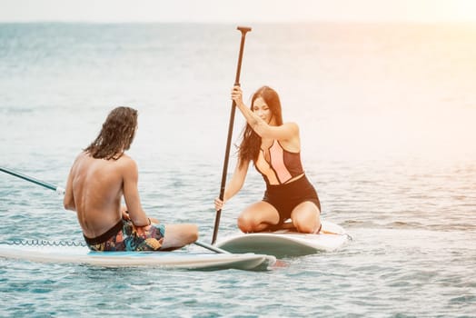 Sea woman and man on sup. Silhouette of happy young woman and man, surfing on SUP board, confident paddling through water surface. Idyllic sunset. Active lifestyle at sea or river