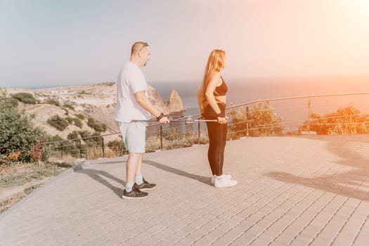 Happy Middle aged couple or friends practicing nordic walking in park near sea. Mature couple with trekking poles walking, practicing Nordic walking outdoors. Aging youthfully and sport concept.