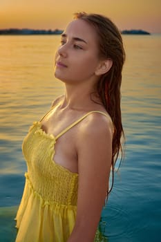 A girl stands in the water against the backdrop of sunrise. A young woman has fun relaxing at the sea. Summer.