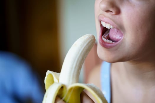 Unrecognizable young girl with mouth open about to eat yummy peeled banana at home