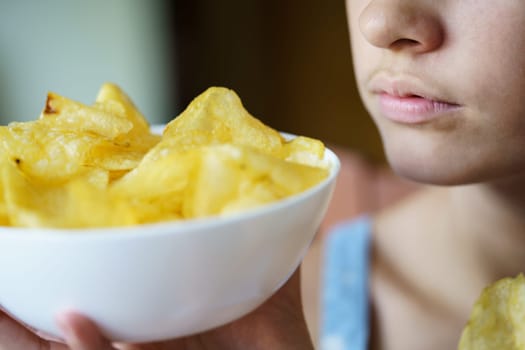 Closeup of crop anonymous teenage girl holding bowl full of potato chips at home