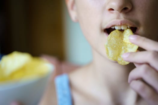 Closeup of unrecognizable young girl eating crispy potato chip at home