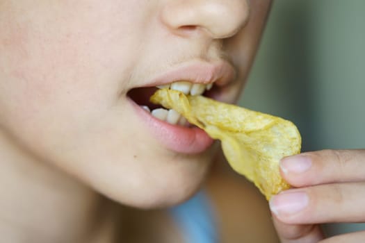 Closeup of crop anonymous young girl biting crunchy potato chip at home