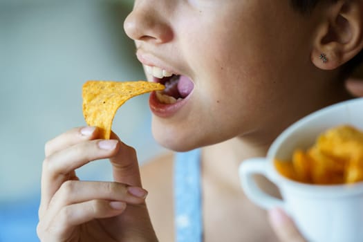 Crop anonymous teenage girl with mouth wide open about to eat yummy nacho chip at home