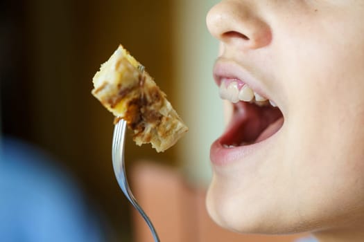 Crop unrecognizable teenage girl with mouth open about to eat yummy potato omelette from fork at home