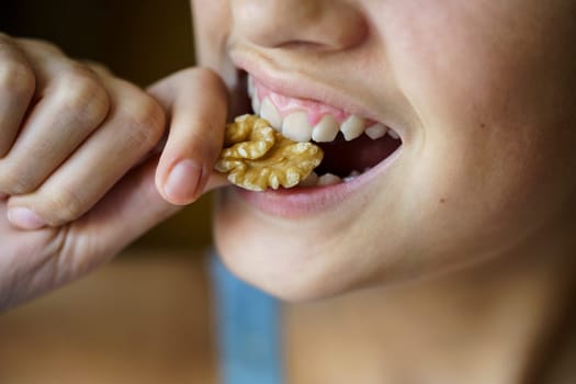 From above closeup of crop unrecognizable teenage girl eating healthy walnut at home