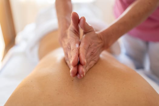 Soft focus of crop anonymous female massage therapist rubbing back of woman with hands clasped during rehabilitation