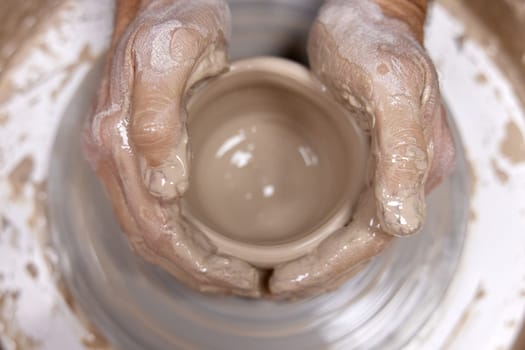 male hands making ceramic cup on pottery wheel, Close-up, top view. man making cup from clay pot