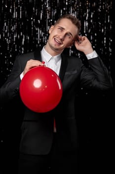 caucasian man in black jacket with red air balloon on dark glitter background. new year party