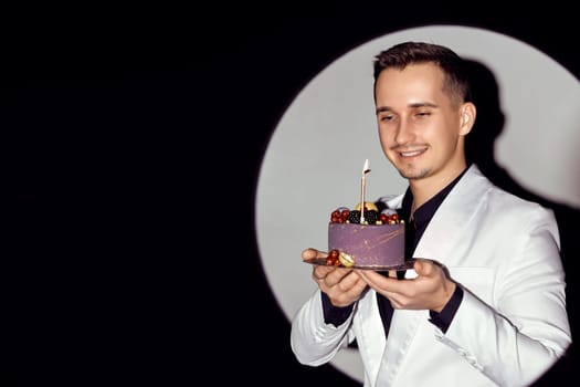 elegant caucasian man in white suit tuxedo holding cake with candle in the circle of light, copy space.