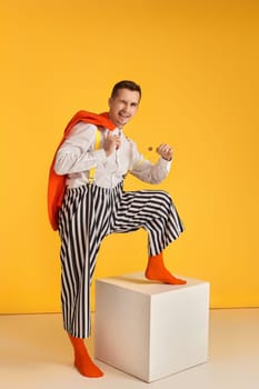 funny crazy guy in orange jacket and striped pants pull his suspenders on yellow background