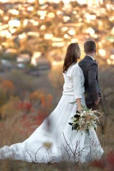 beautiful sensual bride in white wedding dress and groom standing outdoor on natural background