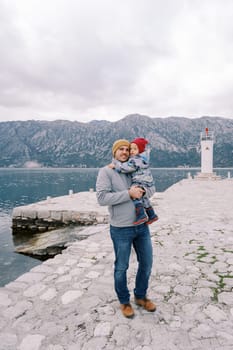 Dad with a little girl in his arms stands on the pier overlooking the lighthouse. High quality photo