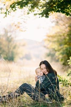 Smiling mother hugging her little daughter sitting on her lap on the lawn. High quality photo