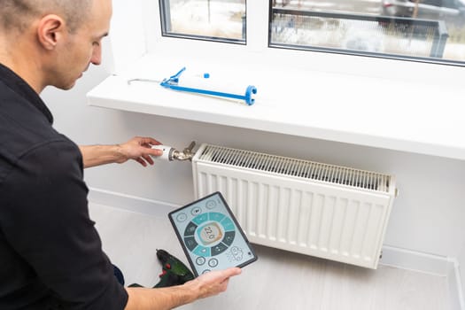 A male plumber installs a radiator in the heating system of an apartment. The guy looks at the phone instructions. Mocap. Panoramic banner. High quality photo