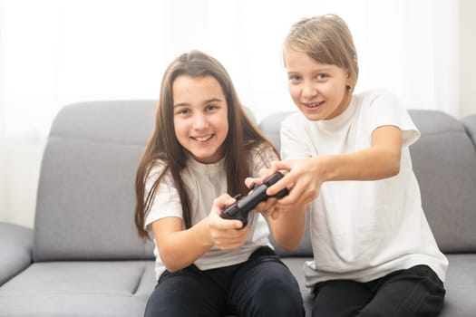 Two sisters kids playing video games at home together. Happy childeren, carefree childhood concept. High quality photo