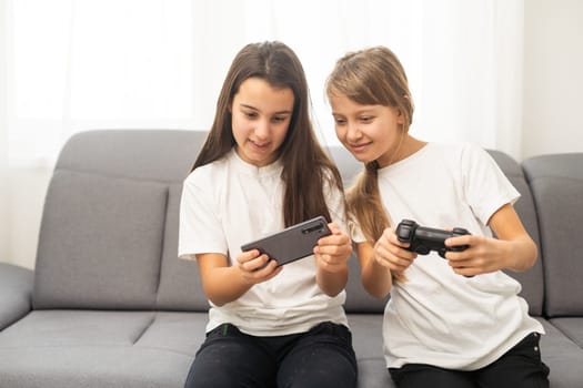 Two little girlfriends playing video game with joysticks. Excited and focused european children. Childhood concept. Entertainment and leisure. Idea of friendship. Grey background in studio. Copy space. High quality photo