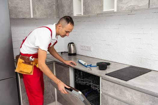Young Repairman Service Worker Repairing Dishwasher Appliance In Kitchen. High quality photo