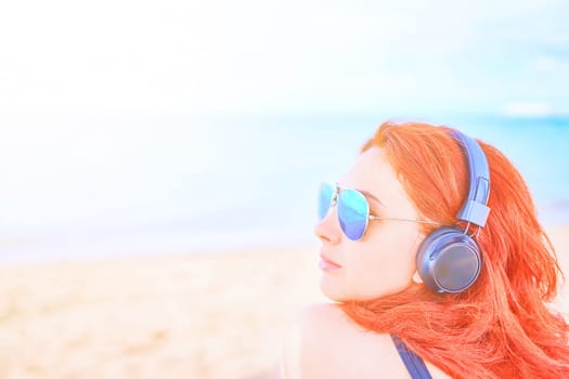 Elegant woman listening to music on the beach. Young female listening to music with headphones.