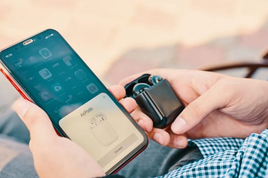 Bishkek, Kyrgyzstan - October 10, 2019: Man holds custom black airpods and connects them to iphone 11