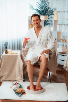 Beauty or body treatment spa salon vacation lifestyle concept with man wearing bathrobe relaxing with drinks in luxurious hotel spa or resort room. Vacation and leisure relaxation. Quiescent