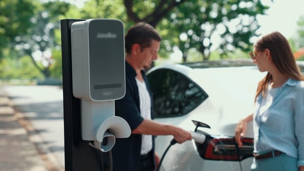 EV car recharging electricity for battery by lovey couple traveling during their road trip travel by eco friendly electric vehicle in national park and greenery forest on holiday. Exalt