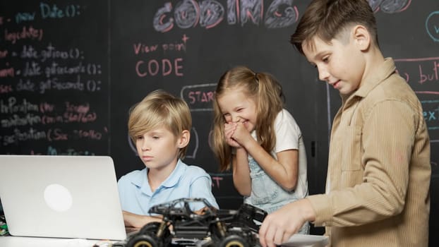 Closeup of boy using laptop programing engineering code and writing program while group of smart diverse student standing surrounded by friend in STEM technology classroom at blackboard. Erudition.