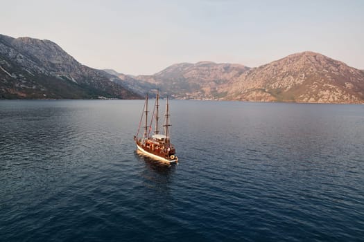 Wooden schooner sails across the sea towards a mountain range on the horizon. Drone. High quality photo