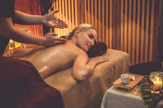 Caucasian woman customer enjoying relaxing anti-stress spa massage and pampering with beauty skin recreation leisure in warm candle lighting ambient salon spa at luxury resort or hotel. Quiescent