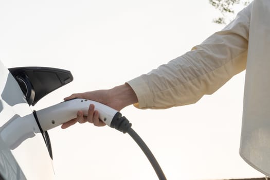 Young woman put EV charger to recharge electric car's battery from charging station. Alternative energy and rechargeable EV car for sustainable environmental friendly travel concept. Expedient