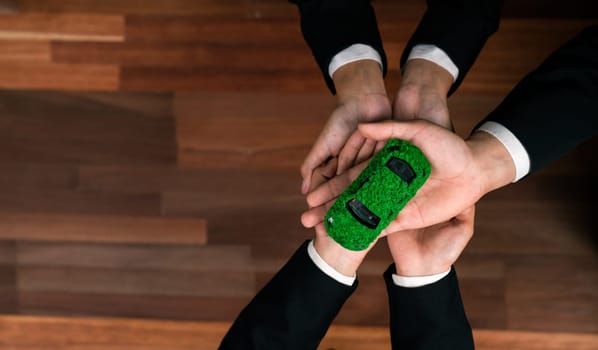 Top view business people holding EV car model as business synergy partnership unite and take action to utilized eco-transportation to reduce CO2 emission for sustainable and greener future. Quaint