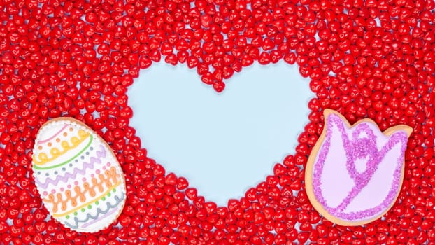 Easter cookies painted with icing with candies with space for text in shape of heart on red heart candies background. Colorful easter cookies on red background. Top View. Copy Space. Spring dessert