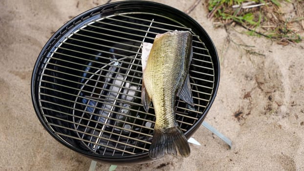 Whole raw fish on the charcoal BBQ grill in camping in summer. Fishing and cooking in forest