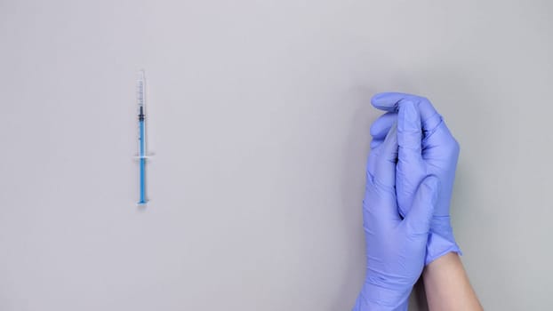 Hand in blue gloves of doctor or nurse holding syringe with liquid vaccine over grey background with copy space. New vaccine. Unknown vaccine. Medical gloves