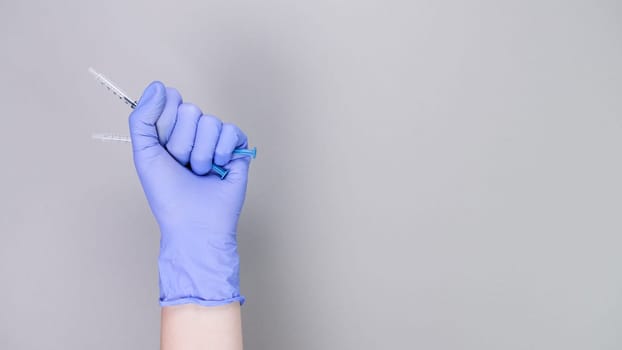 Hand in blue gloves of doctor or nurse holding syringe with liquid vaccine over grey background with copy space. New vaccine. Unknown vaccine. Medical gloves