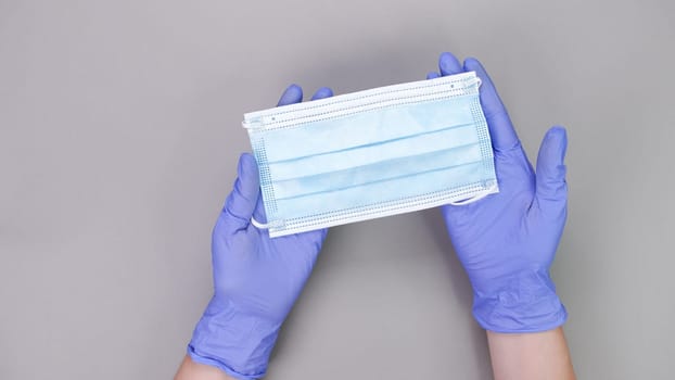 Hand in blue gloves of doctor or nurse holding protective blue face mask over grey background with copy space. New vaccine. Unknown vaccine. Medical gloves