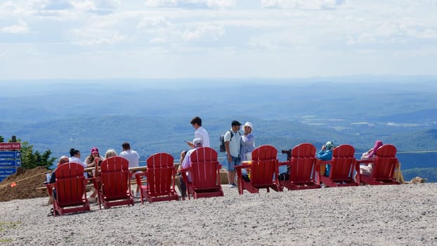 Sightseeing mountain views at Mont Tremblant ski Resort in summer. Tourists enjoying sitting at red chairs at ski resort village. Mont-Tremblant, Quebec, Canada - 22.09.2022.