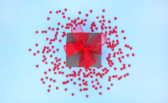 Gift box decorated with red ribbon bow on blue background with red candies. St. Valentine Day. Love, gift concept