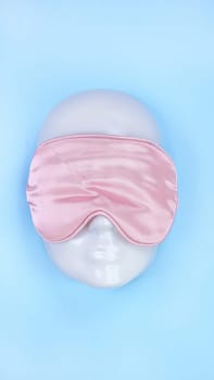 Pink sleeping eye mask on white mannequin face on blue background, sleeping disorder. Valentine day. Holidays, Head accessory. Plastic face