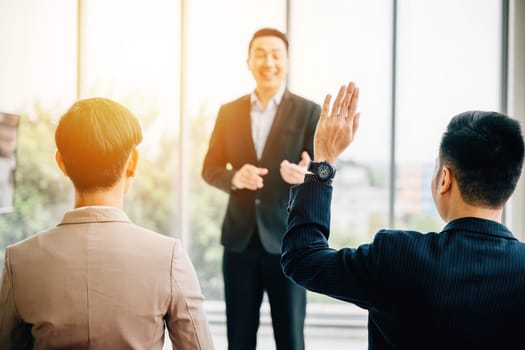 In a conference, business professionals raise their hands to ask questions, vote, or volunteer, reflecting audience engagement and effective teamwork in a corporate setting.
