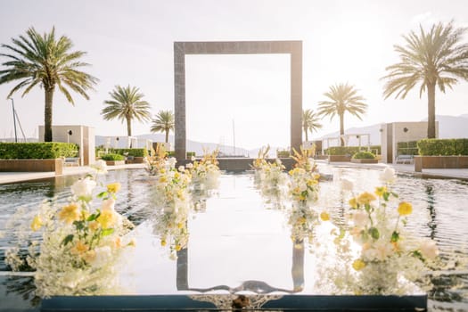 Bouquets of flowers stand in rows in a long pool with a square arch in the center. High quality photo