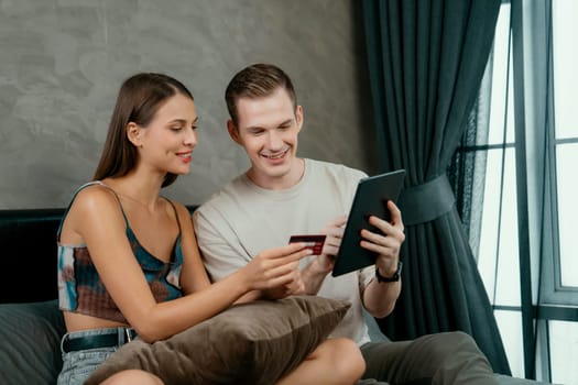 Young couple sit in the home bedroom using online payment app and digital wallet on smartphone to pay with credit card. E commerce shopping and modern purchasing via mobile internet. Unveiling