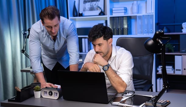 Stressful business partner with headache analyzing paperwork project together on desk at night time of startup product company. Concept of overworked design on neon blue light modern office. Sellable.