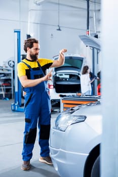 Serviceman in repair shop using augmented reality holograms to check car condition during maintenance. Garage employee using futuristic AR technology to examine out of order vehicle